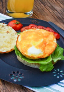 Breakfast egger sandwich with the top off it, egg showing on top of lettuce, on a black plate.