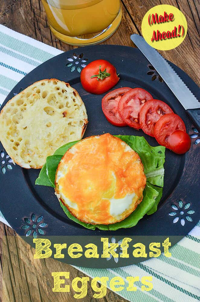 A breakfast egger sandwich with tomatoes on the side on a black plate.