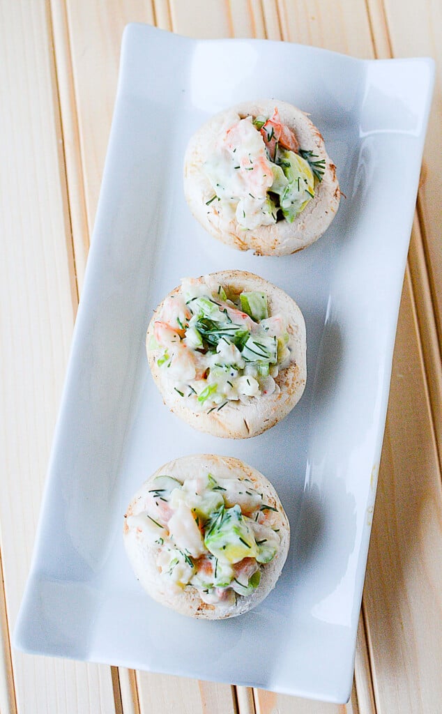 A top down photo of three mushrooms containing shrimp and avocado salad, sitting on a white plate.