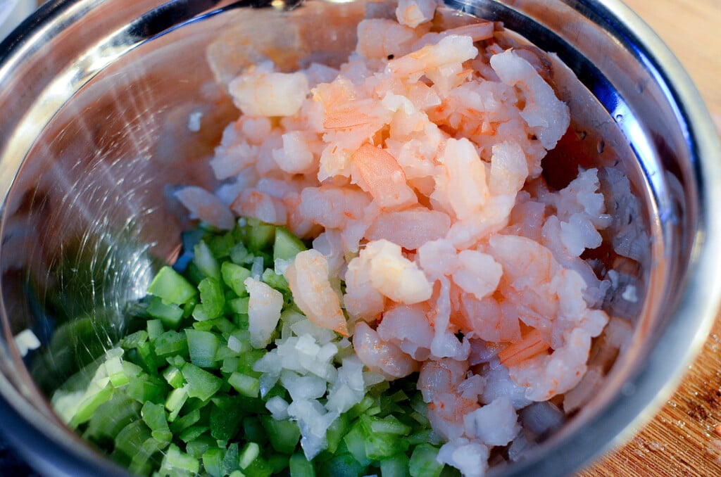 A sliver mixing bowl containing shrimp, onion and green pepper with celery.