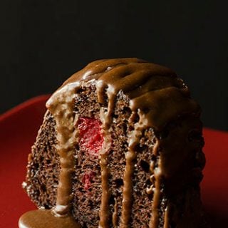 A piece of chocolate cake with icing dripped over the top on a red plate.