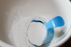 A blue 1cup measuring cup filled with flour sitting in the bottom of a bowl