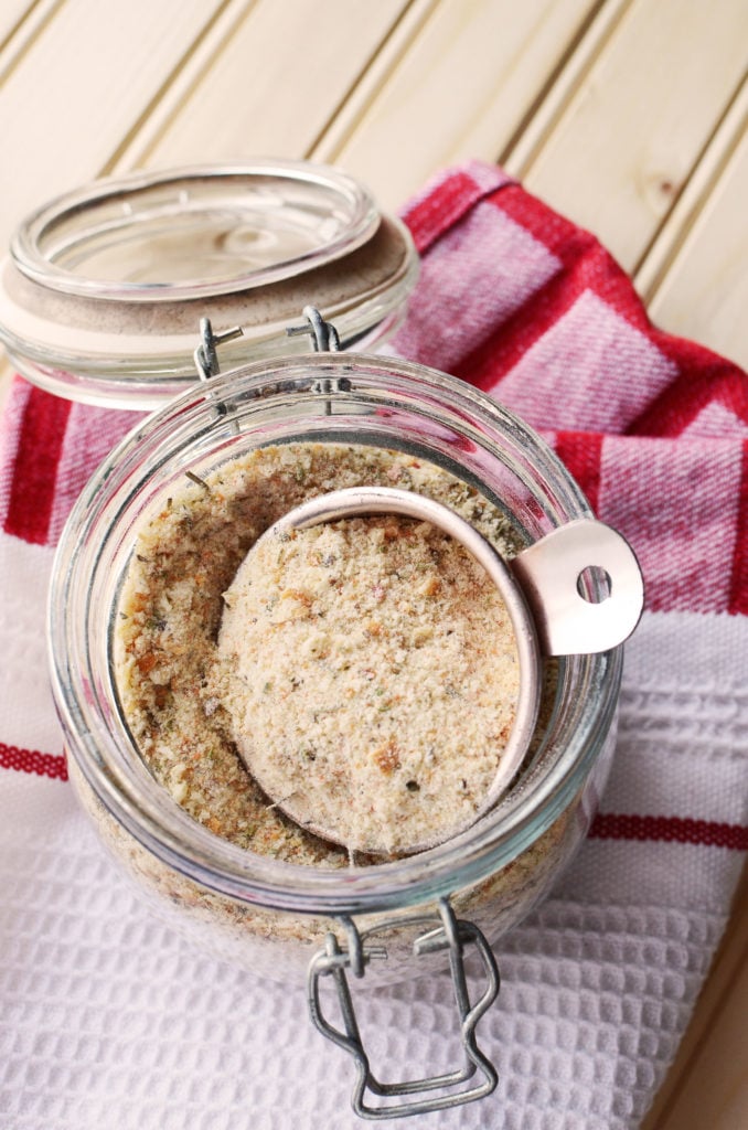 A pretty jar filled with seasoned breadcrumbs on a red cloth.