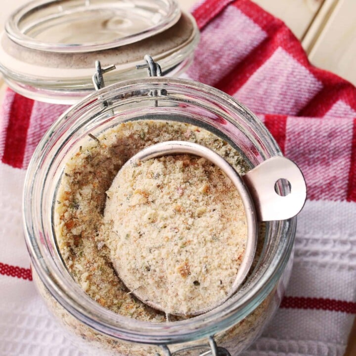 A pretty jar filled with seasoned breadcrumbs on a red cloth.