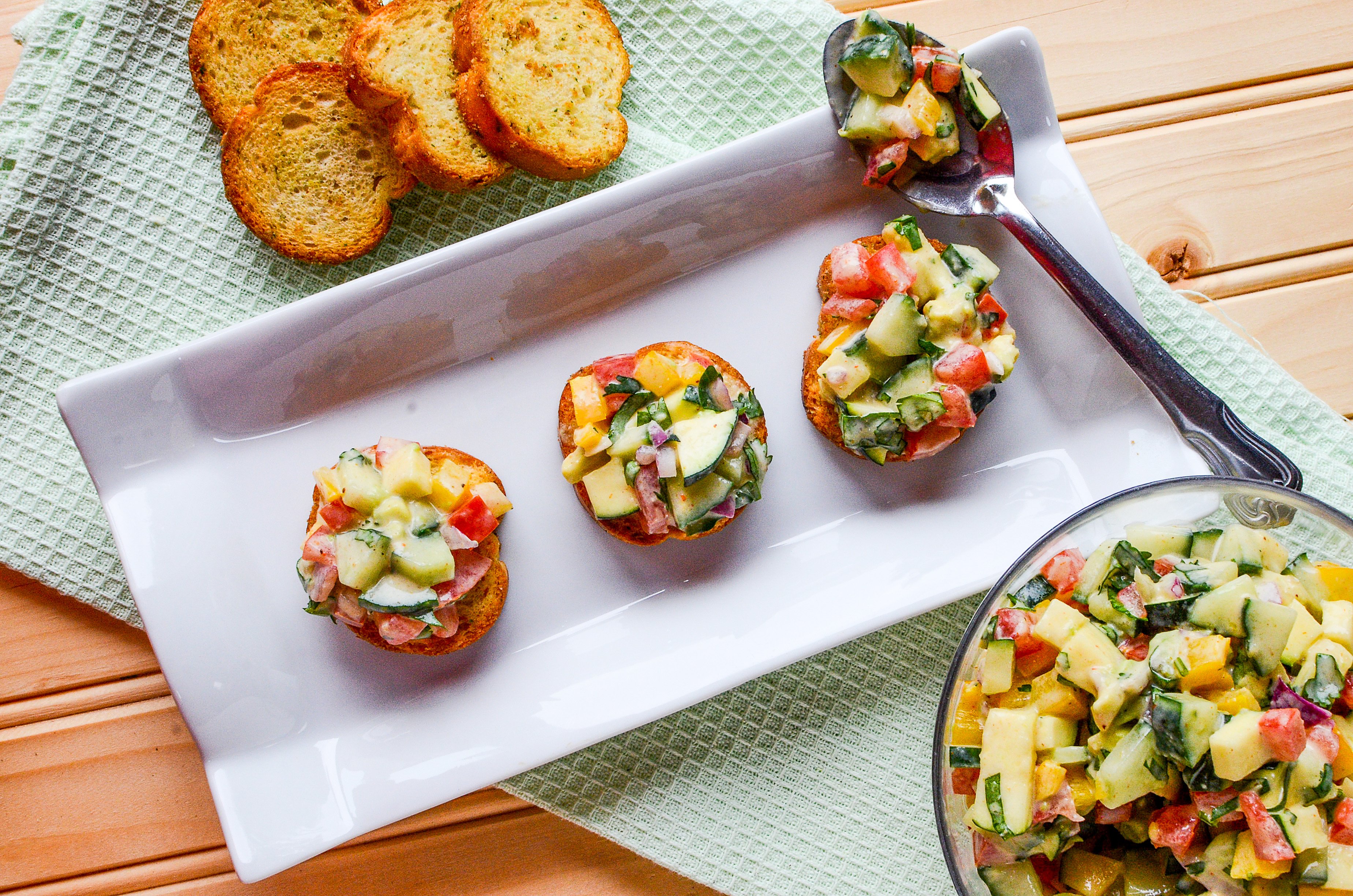 A top down photo of a Cucumber avocado salsa on small baguettes and a white plate.