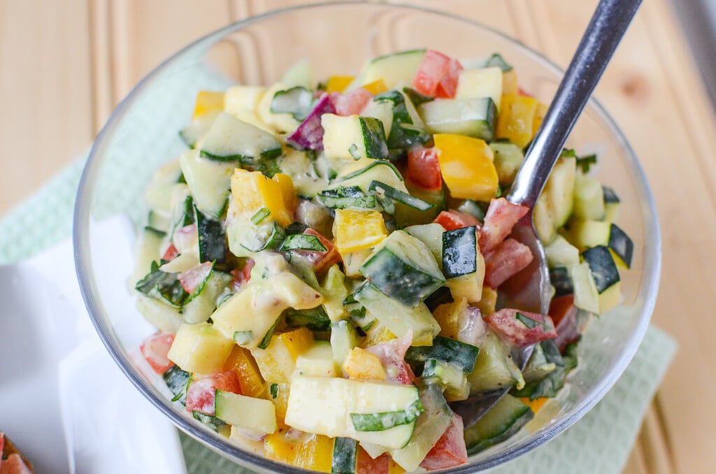 Fresh vegetable salsa in a glass bowl with a spoon sticking out of it.