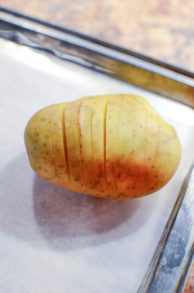 A potato sliced in many slices on an baking sheet.