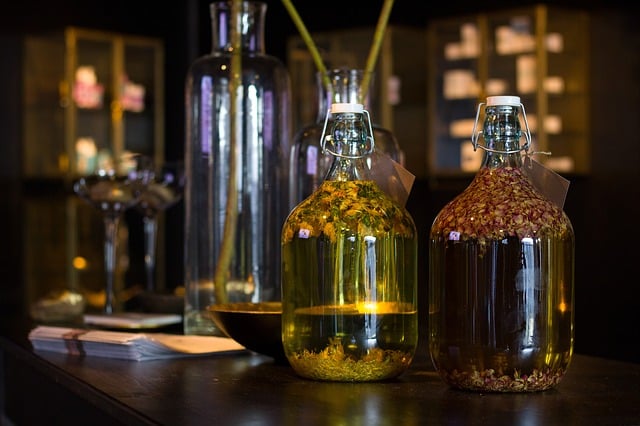 2 glass bottles filled with dried herbs, sitting on a dark talbe with cabinets in the background.