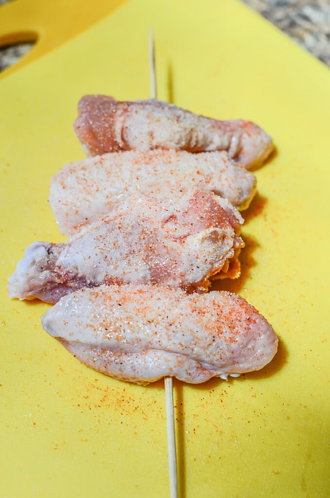 Raw seasoned chicken wings on a wooden skewer.