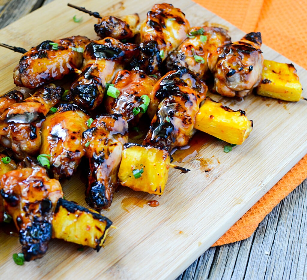 Chicken wings grilled on skewers with pineapple chunks on the end of the skewer.