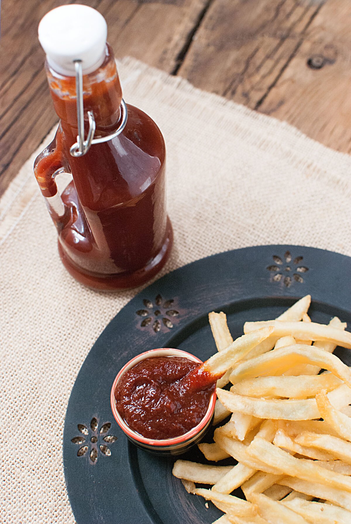 Ketchup in a bottle with fries on a plate. A small amount of ketchup is in a bowl on the plate as well.