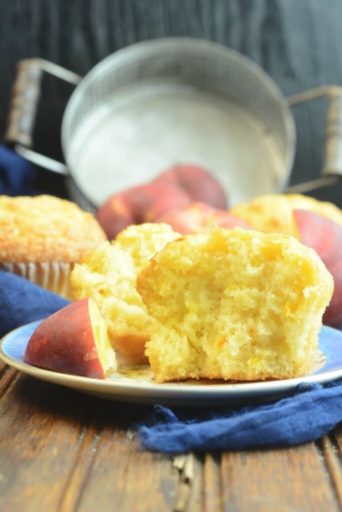 Peach muffins on a blue plate with a slice of peach beside it.