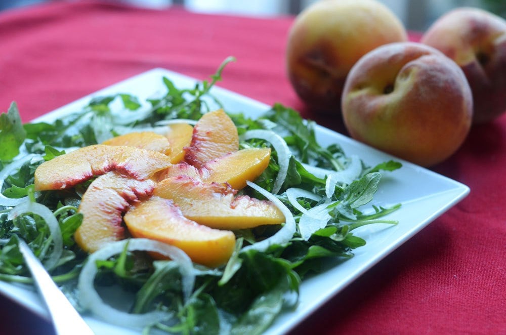Sliced peaches on top of arugula greens with peaches on the background.