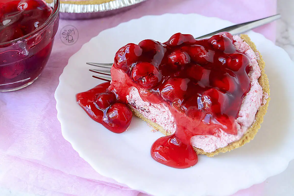 A slice of the cherry pie on a plate with a fork on the right of it, at the top.