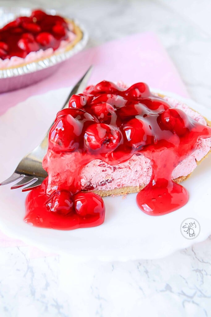 A piece of cherry pie on a white plate with a fork on the left of the slice.