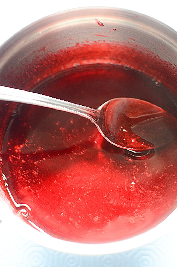 Jello being made in a bowl with a spoon inside the mixture.
