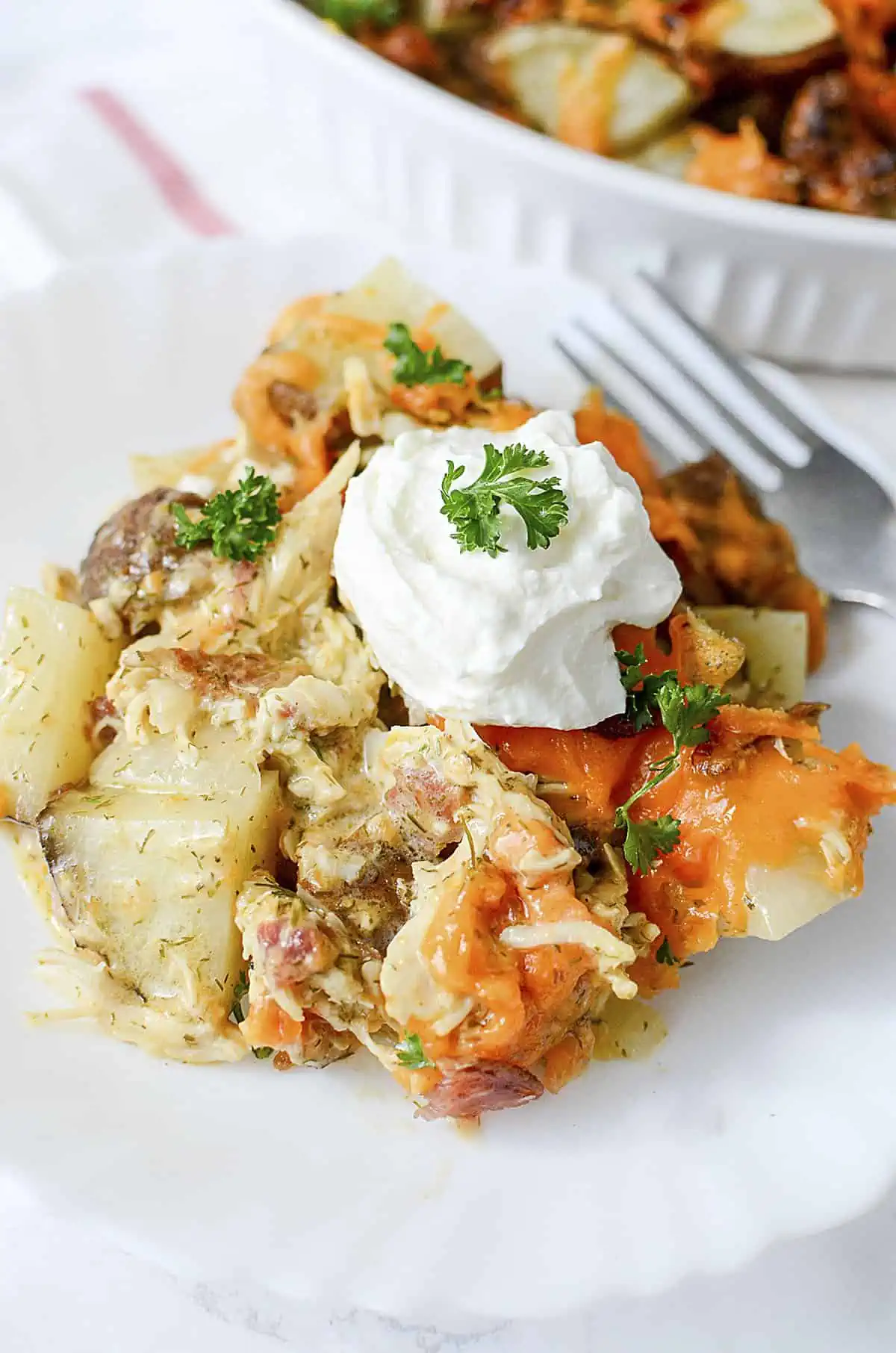 A serving of the bacon ranch potato bake on a white plate with sour cream dolloped on top.