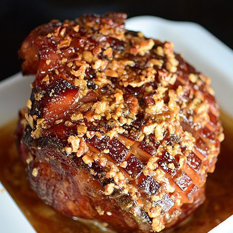 A large ham with a brown sugar pecan glaze over the top, sitting in a white baking dish.