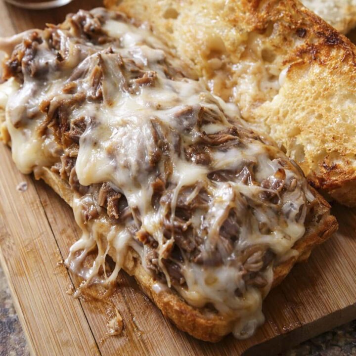 Mississippi pulled pork dip sandwiches on a wooden cutting board.