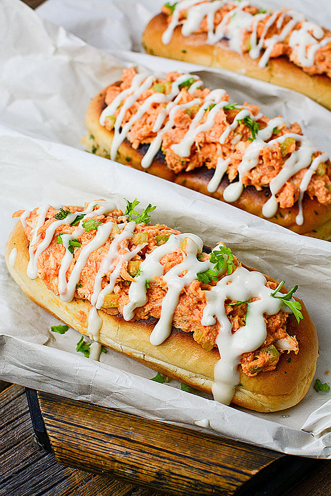 Buffalo chicken stuffed buns drizzled with ranch on wood tray.