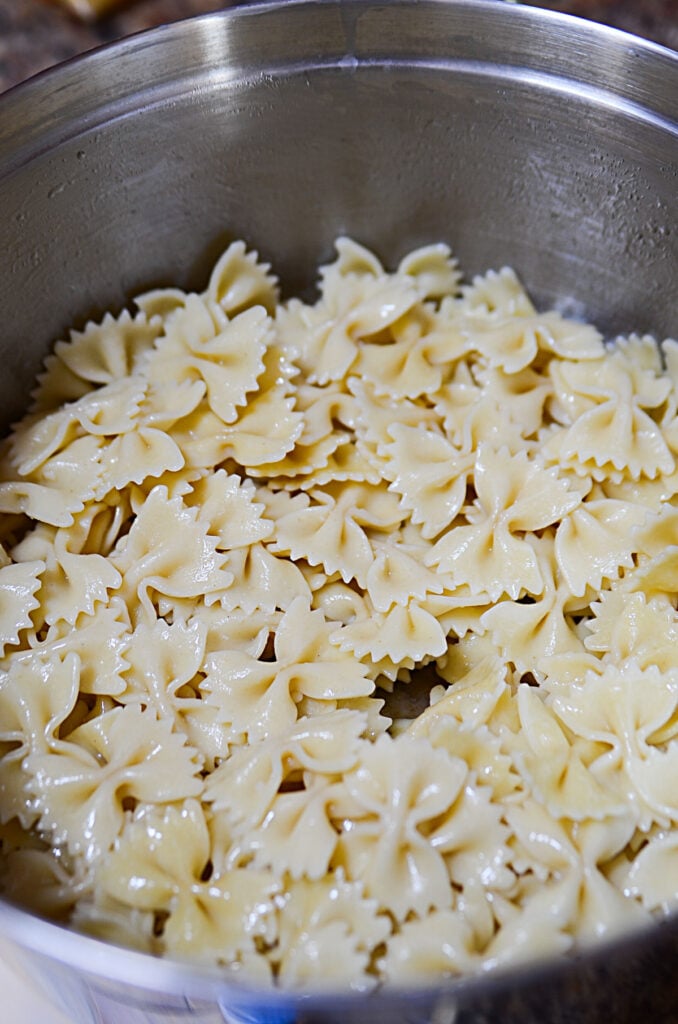 Bow tie pasta that's been cooked, sitting in a silver bowl to cool. 