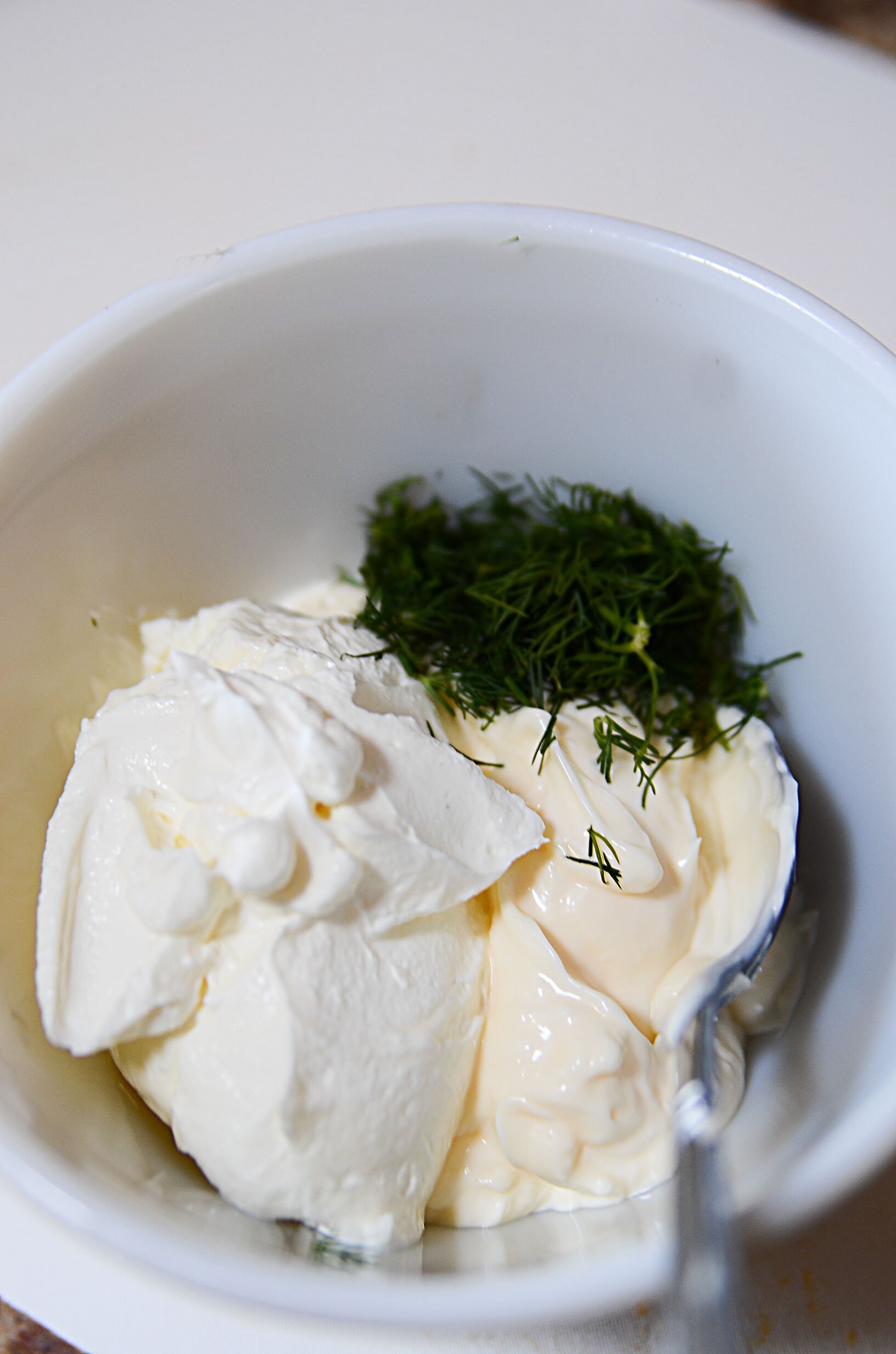 A white bowl with sour cream, fresh dill, mayo and pickle juice, ready to be mixed into a dressing. 
