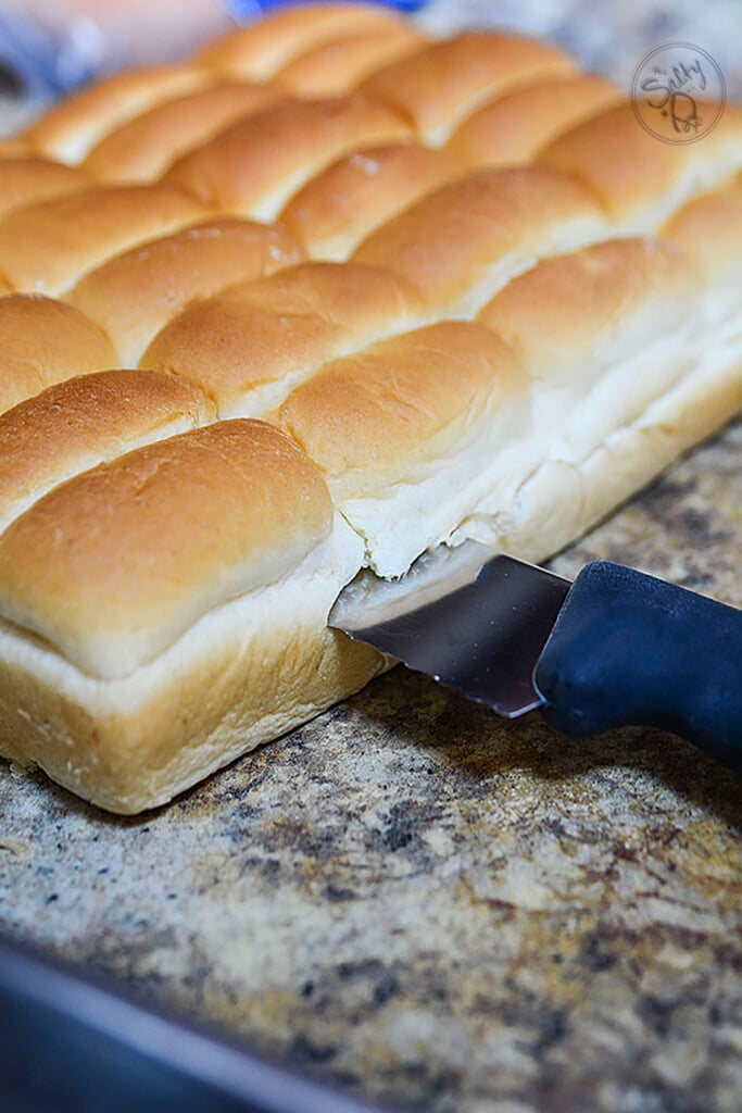 A knife cutting the tray buns horizontally.