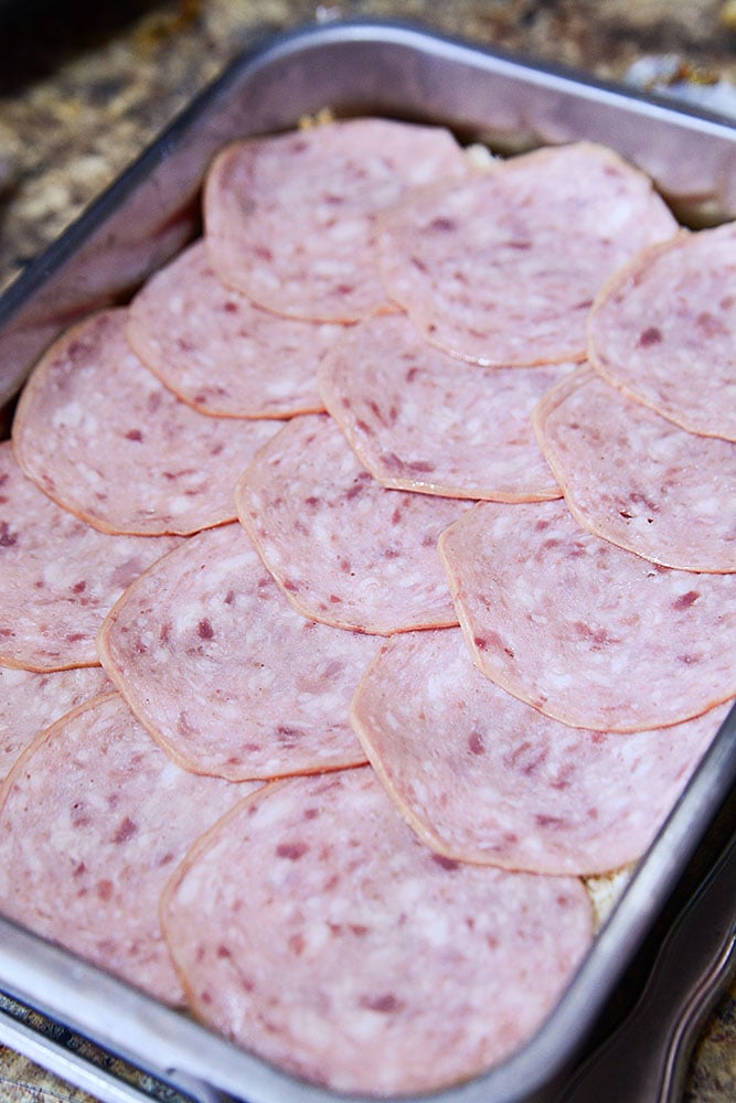 A photo of some of the deli meats being placed on the buns.