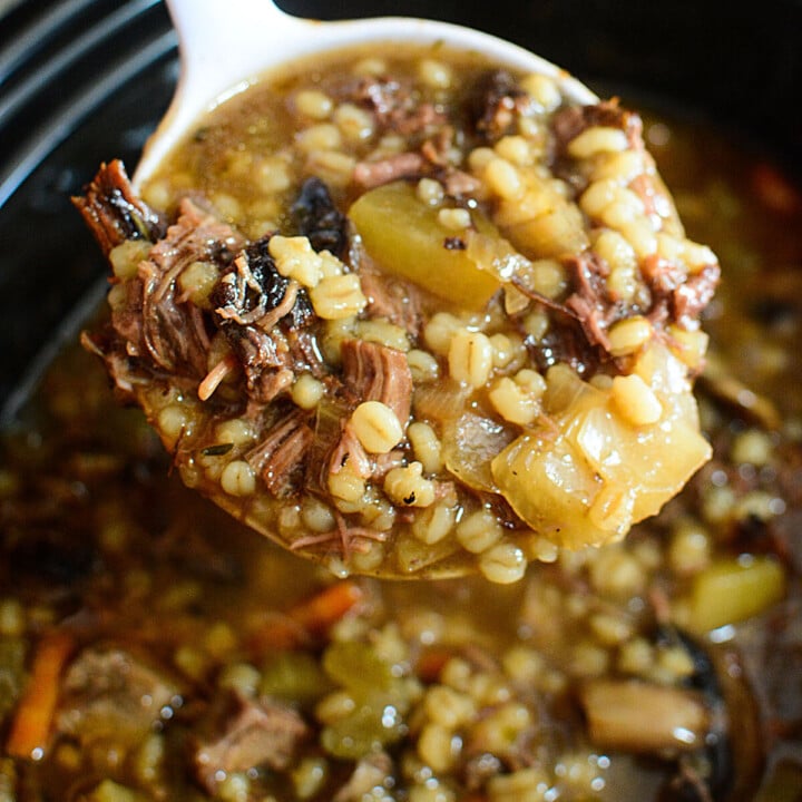 A white ladle full of slow cooker beef barley stew.