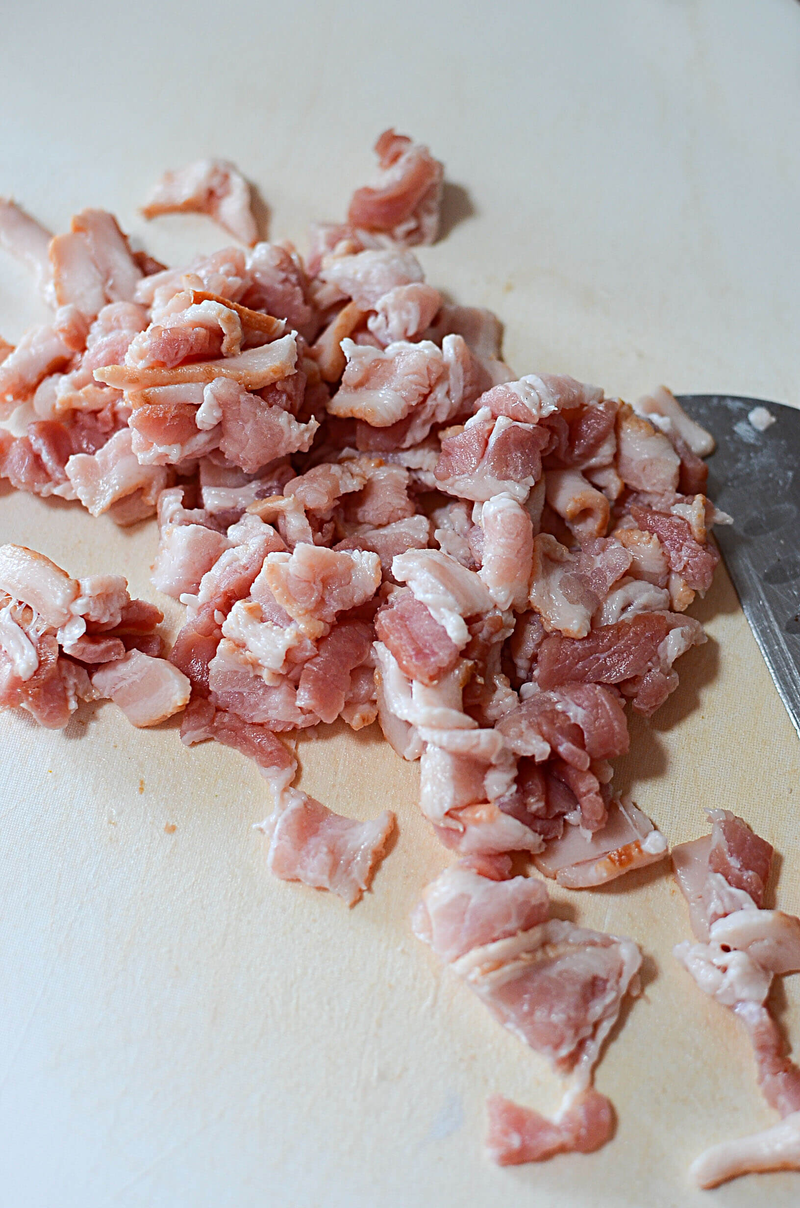 Diced bacon on a white cutting board with a knife on the right.
