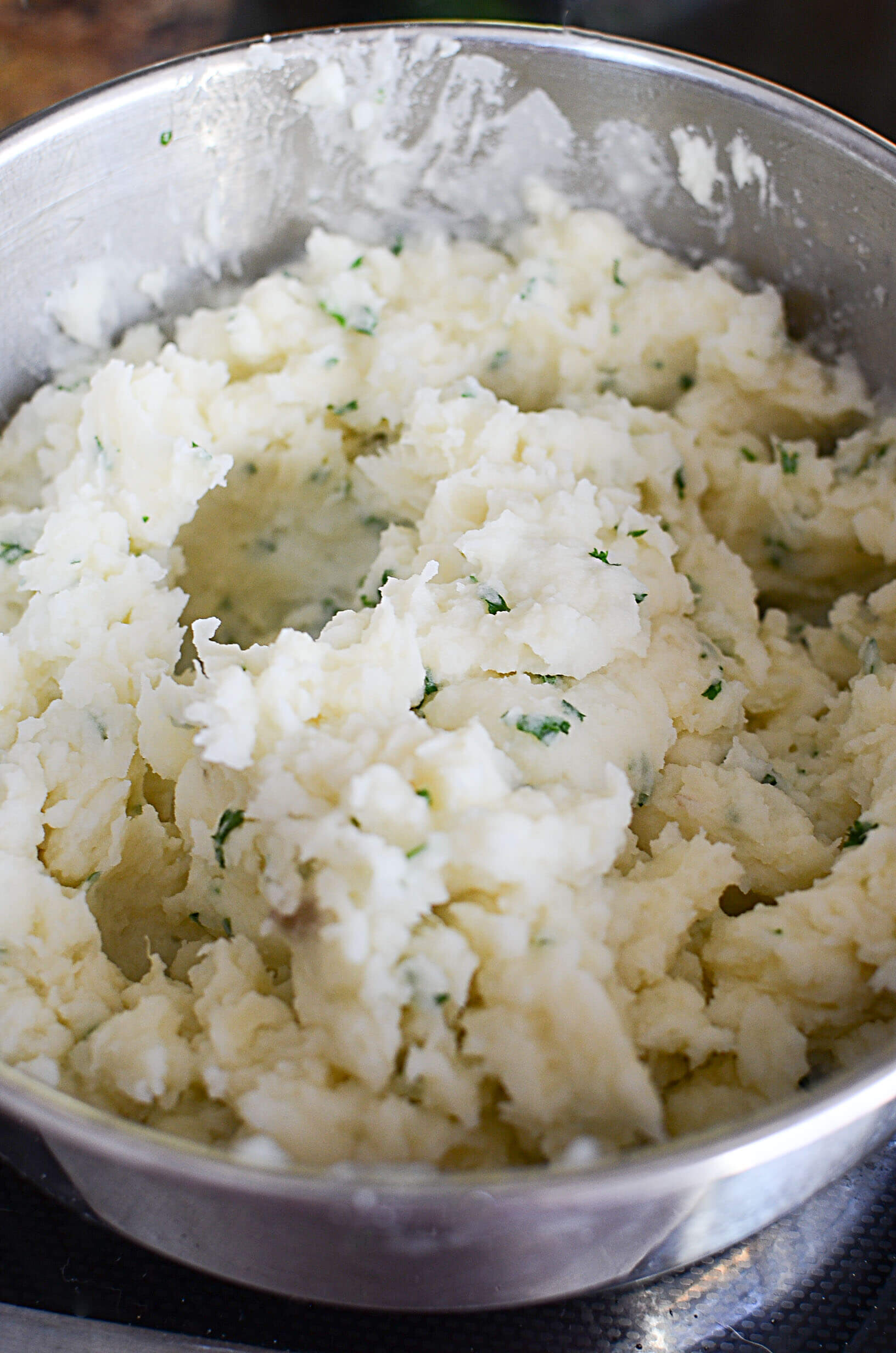 Cooked and mashed potatoes in a silver bowl with herbs. 