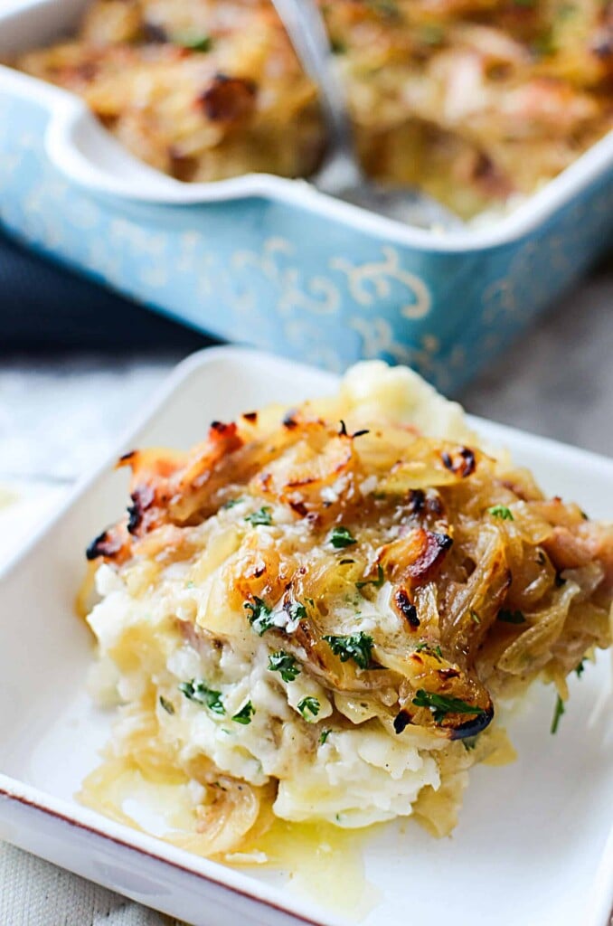 Mashed potatoes with buttery onions and bacon on the top in a white dish.