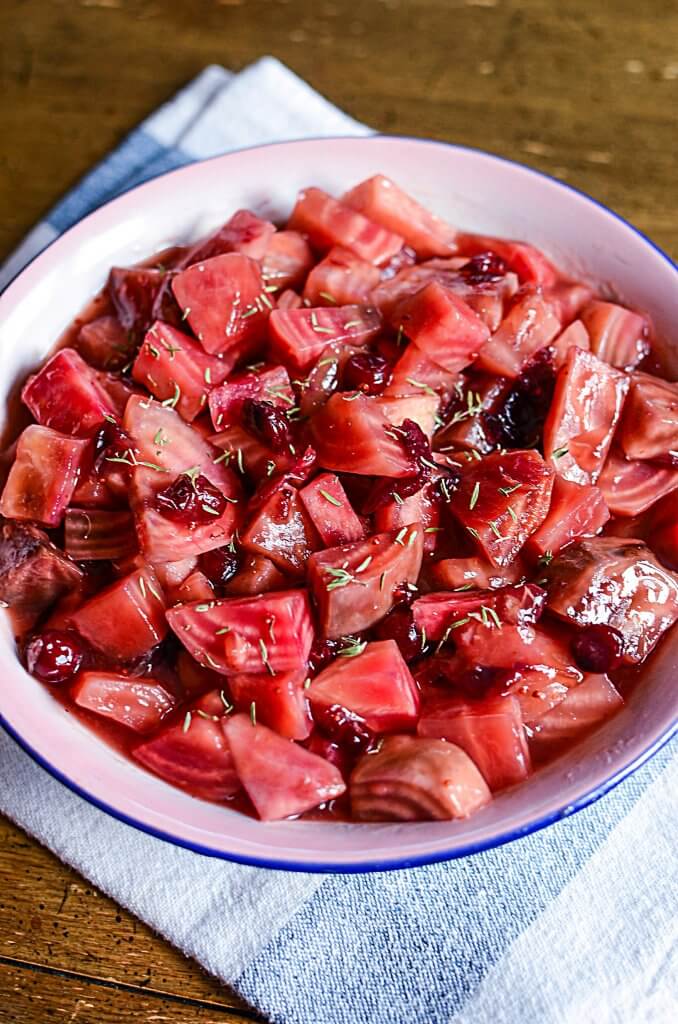 In this top down photo, candy cane beets are served in a blue rimmed bowl with cranberries nestled beside the beets. 