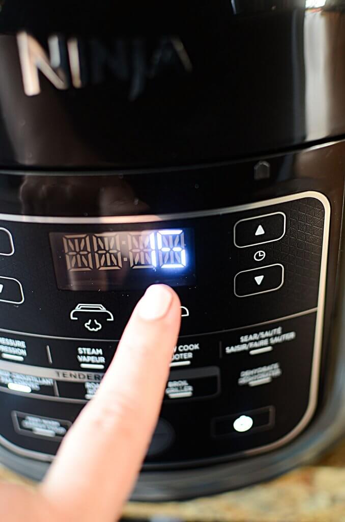 An image of a Ninja Foodie with an index finger pressing one of the buttons of the settings showing the number 15