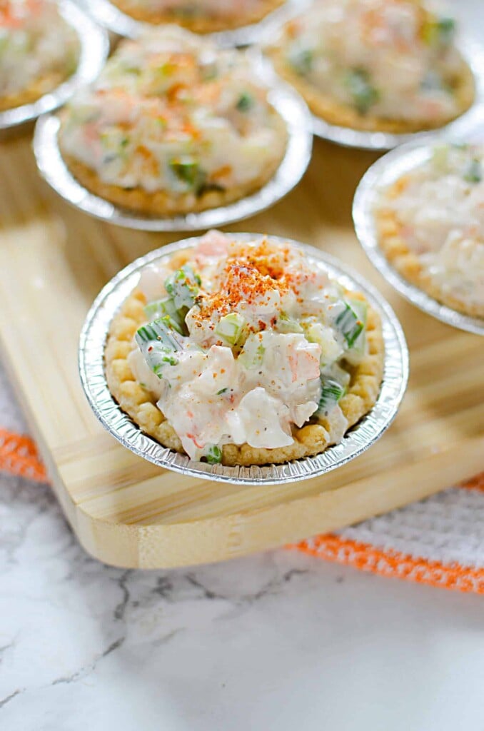 A 45 degree angle shot of a few shrimp and asparagus tarts on a cutting board with an orange and white napkin underneath. 