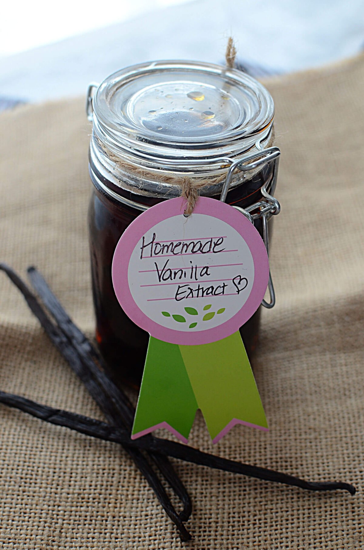 Homemade vanilla extract in a glass jar with vanilla pods next to it.