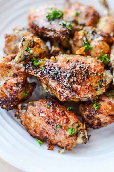 Garlic Parmesan Wings piled on a white plate with parsley.