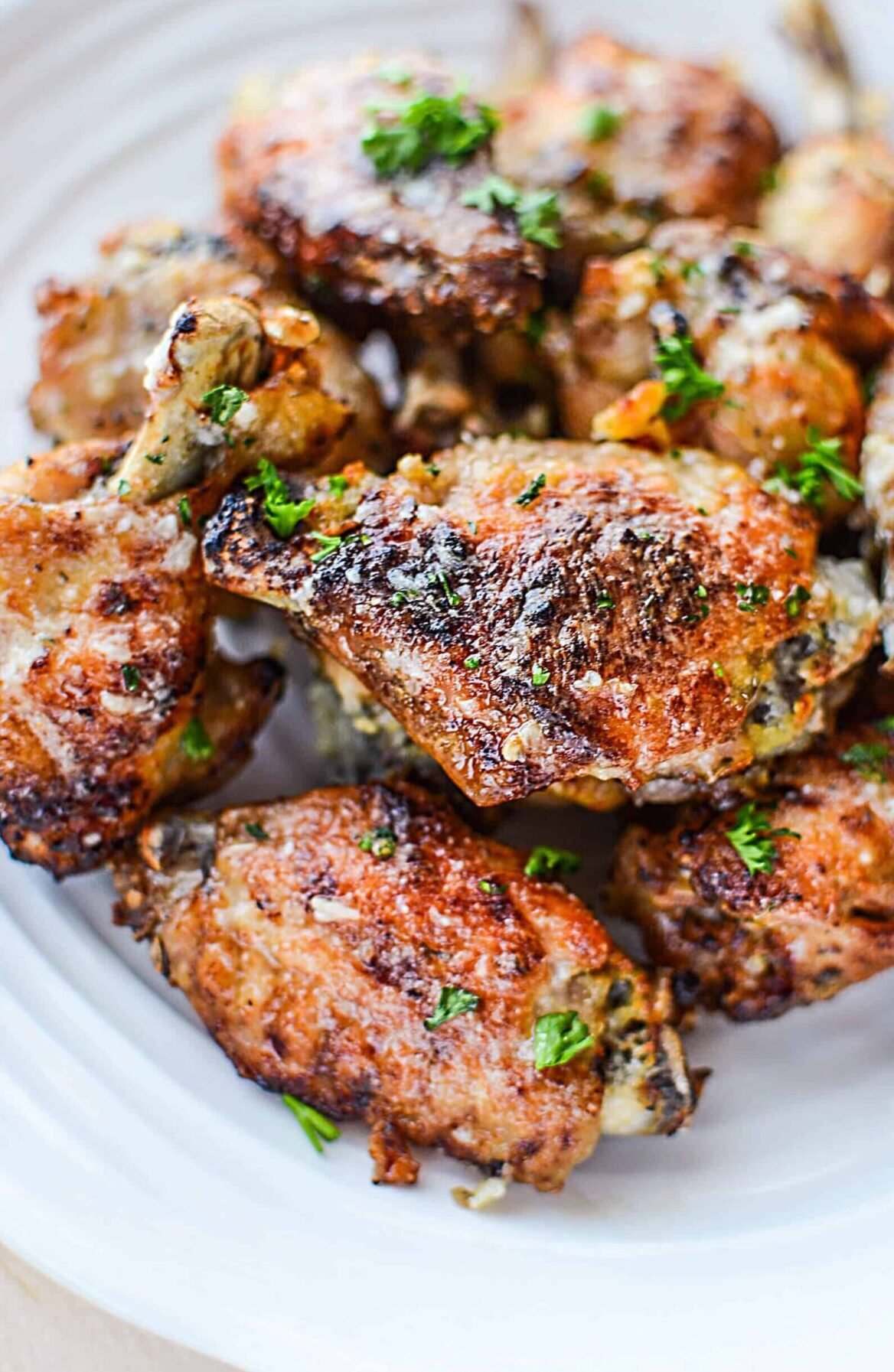 Garlic Parmesan Wings piled on a white plate with parsley.