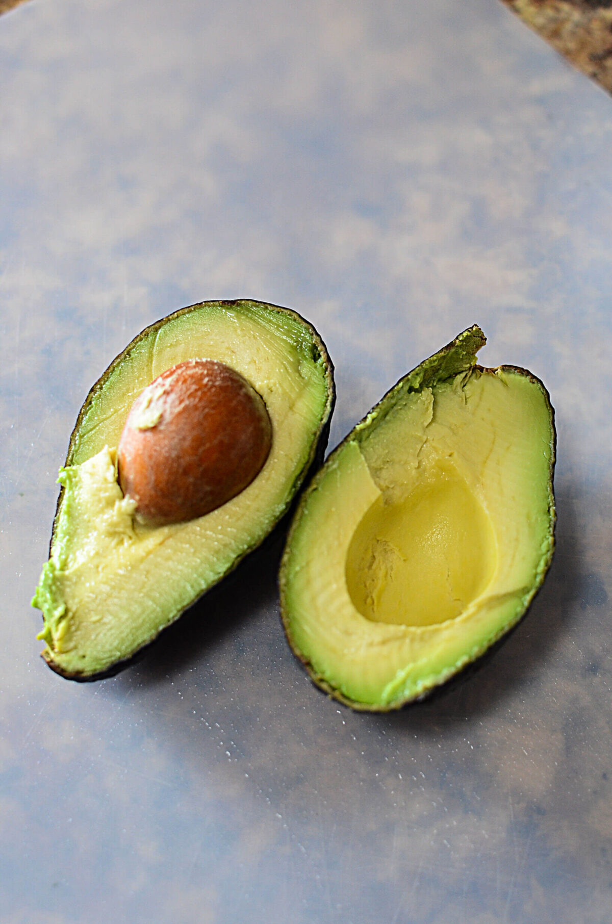 An avocado cut in half on a white cutting board.