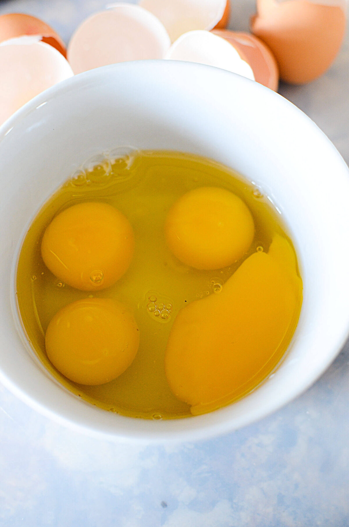 4 eggs in a white bowl with shells at the top of the image.
