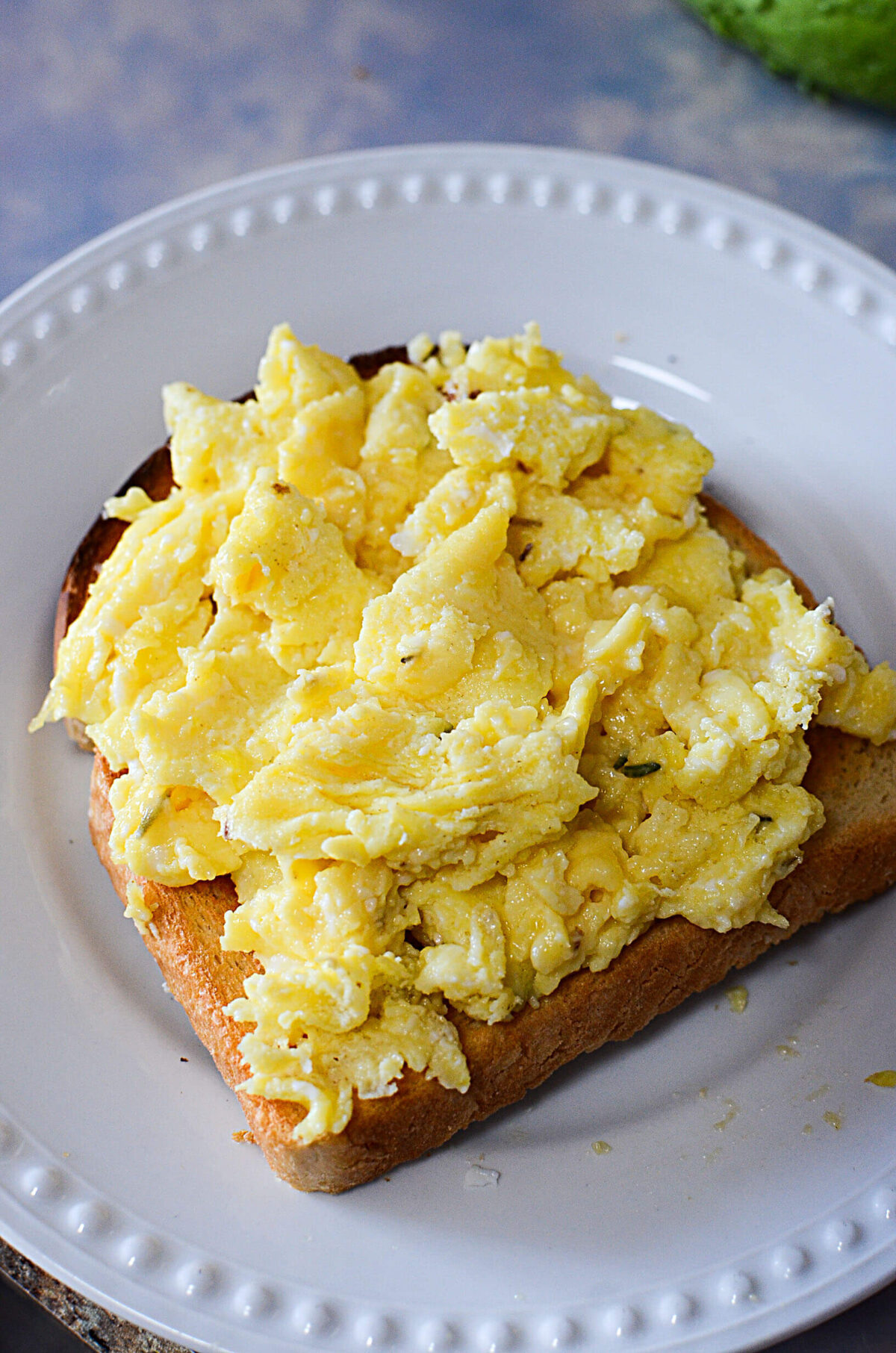 Scrambled eggs sitting on toast, on a white plate.