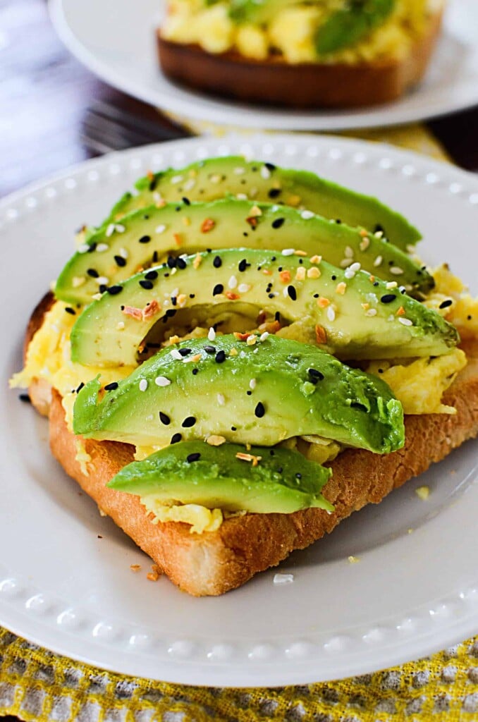 Sliced avocado on top of scrambled eggs on a piece of toast.