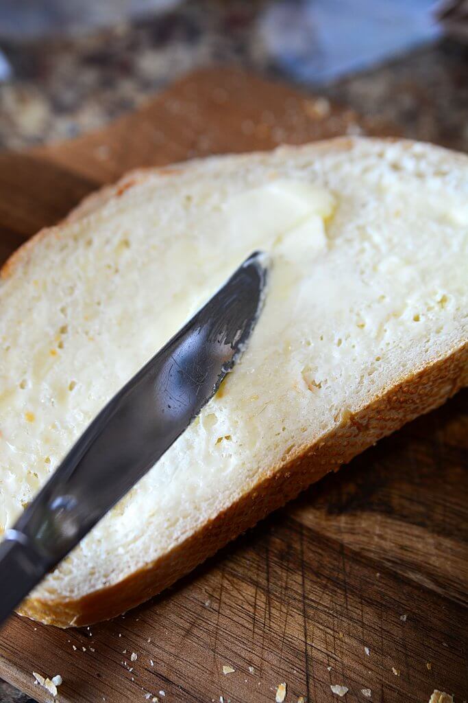 A knife buttering  a piece of bread.