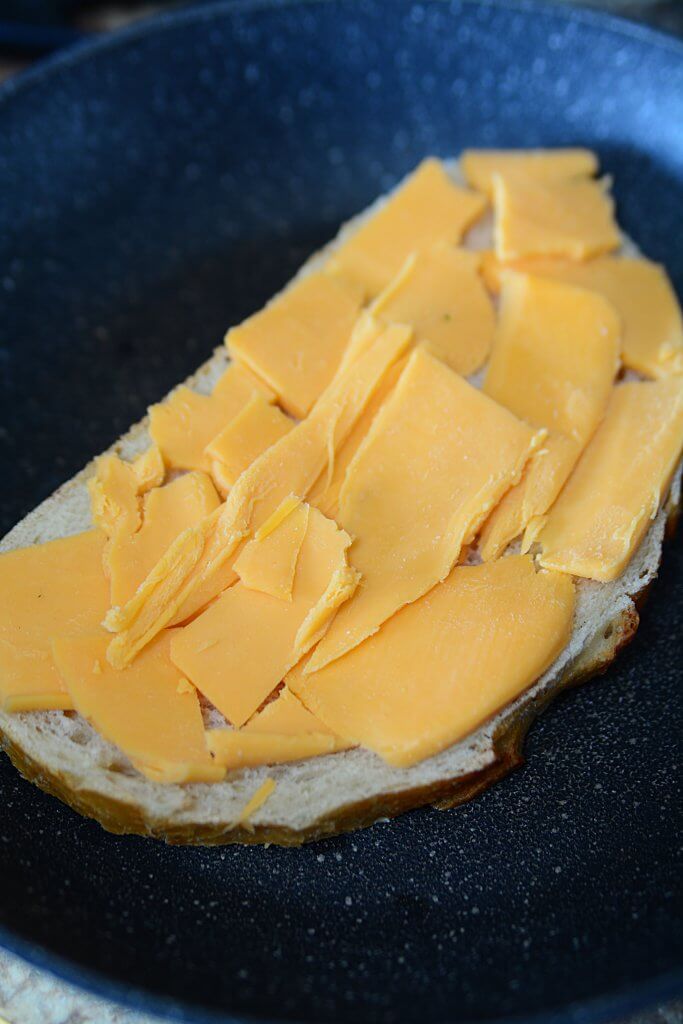 Thinly sliced pieces of cheddar on a piece of bread sitting in a frying pan.