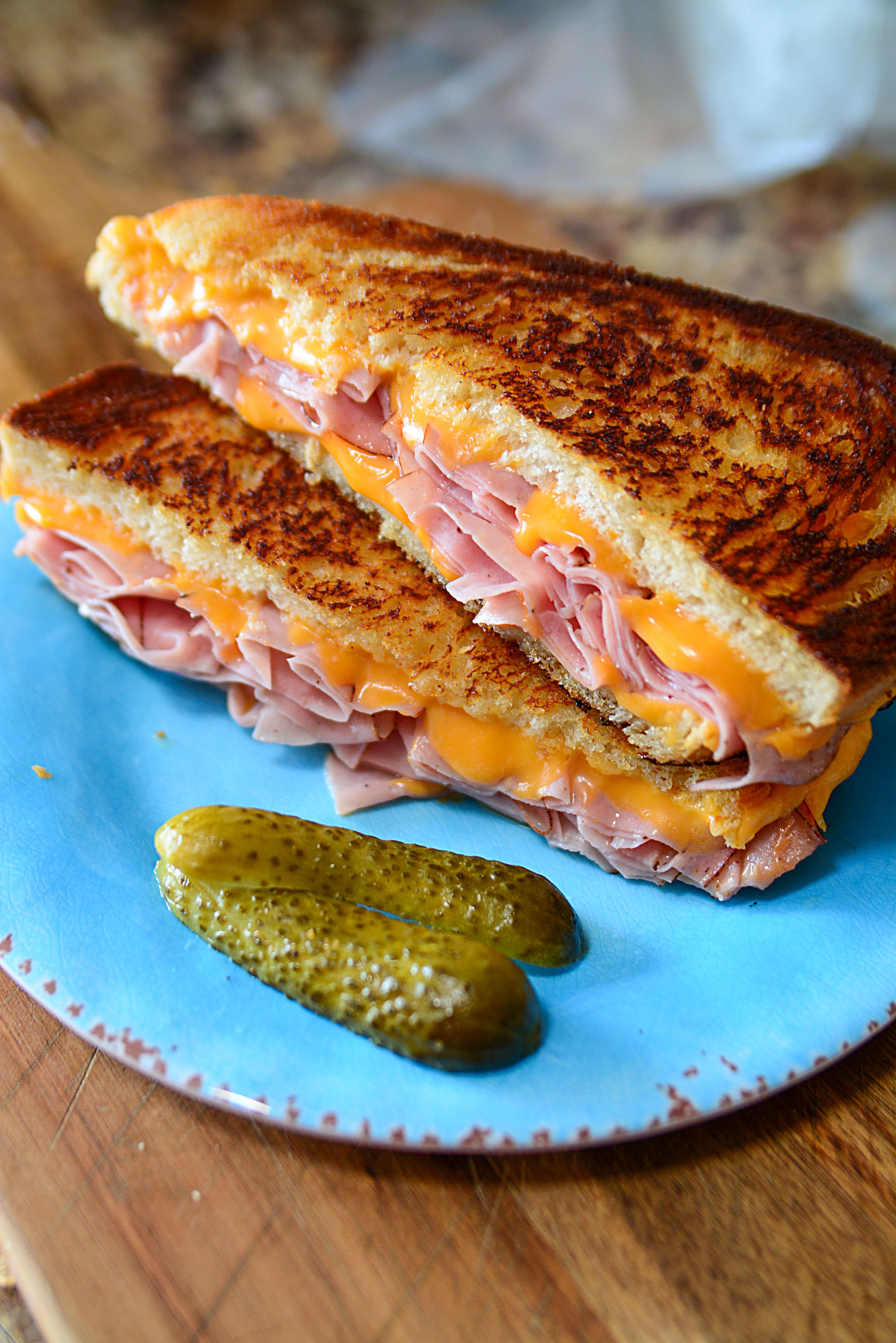 Two halves of a sandwich on top of eachother with a pickle in the foreground.