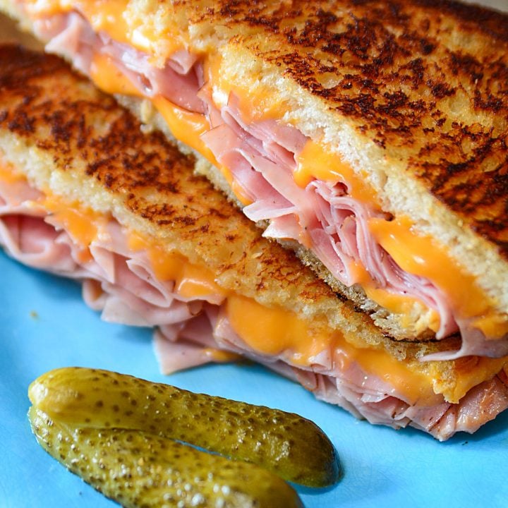 A grilled ham and cheese sandwich cut in half sitting on a blue plate.