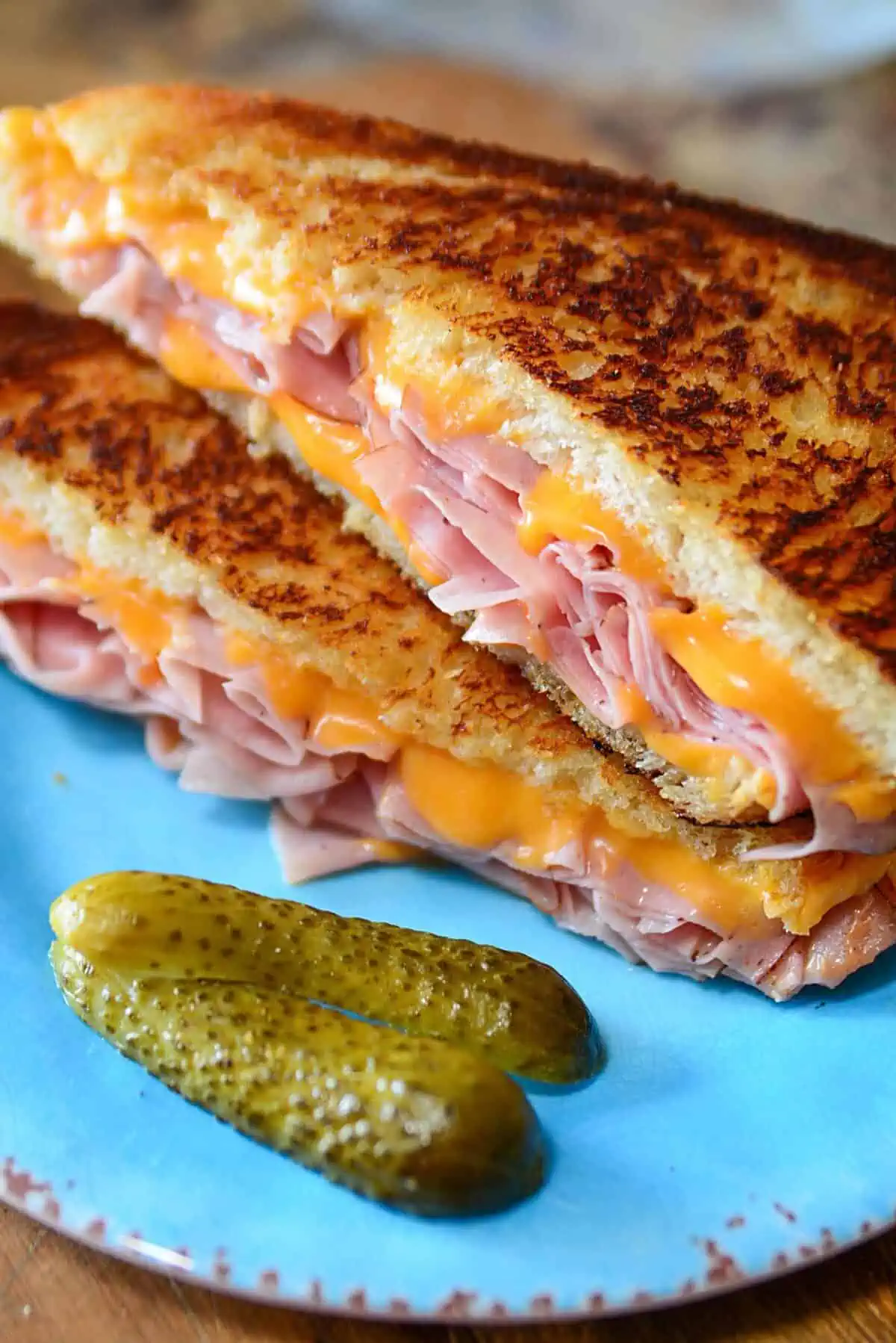 A grilled ham and cheese sandwich cut in half sitting on a blue plate.