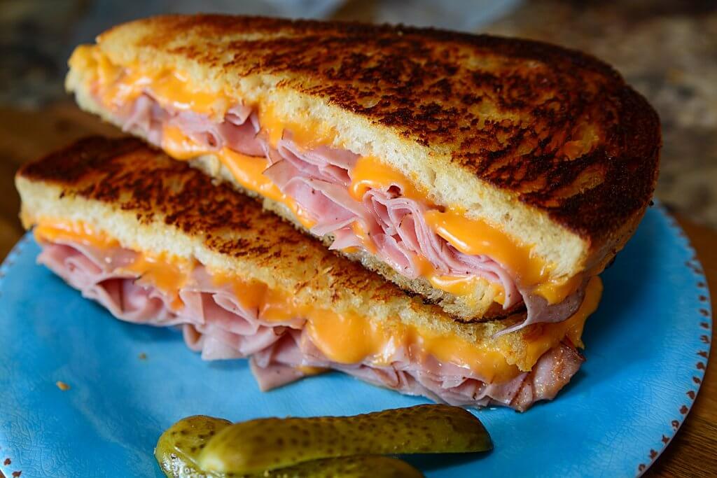 The grilled ham and cheese sandwich cut in half, with cheddar and deli ham in the center on a blue plate.