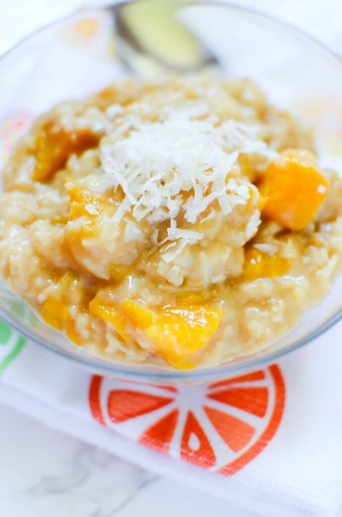 Steel cut oats with pieces of juicy peaches in a glass bowl topped with shredded coconut. The napkin underneath has a picture of a red citrus slice that makes you think of the tropics with this breakfast!