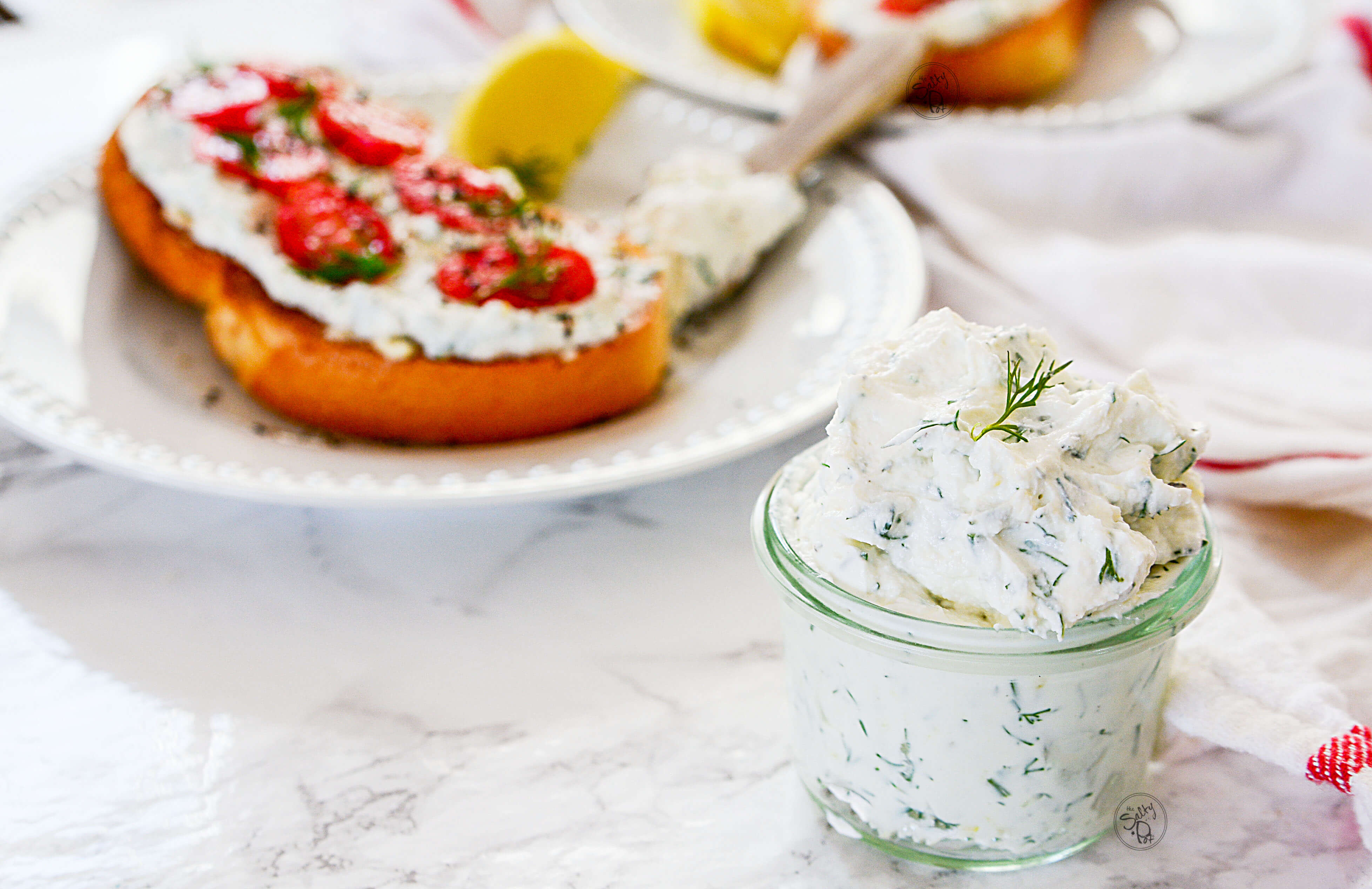 The dill spread is in the front right of the photo with a piece of toast with cheese and tomatoes is in the background on the left. 